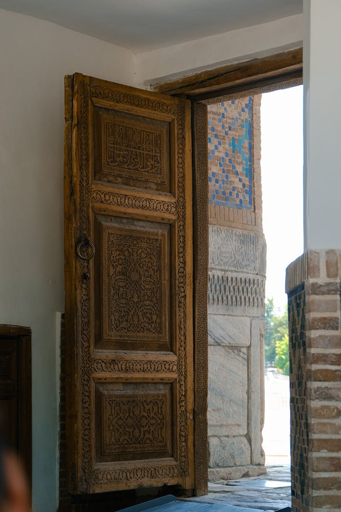 An intricately carved wooden door opens to a mosaic-tiled entrance, showcasing artistic craftsmanship.